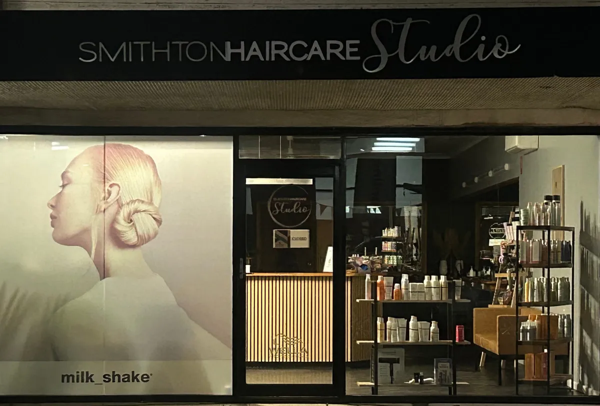 The Nelson Street shopfront of Smithton Haircare Studio, lit from inside with the studio sign above the window